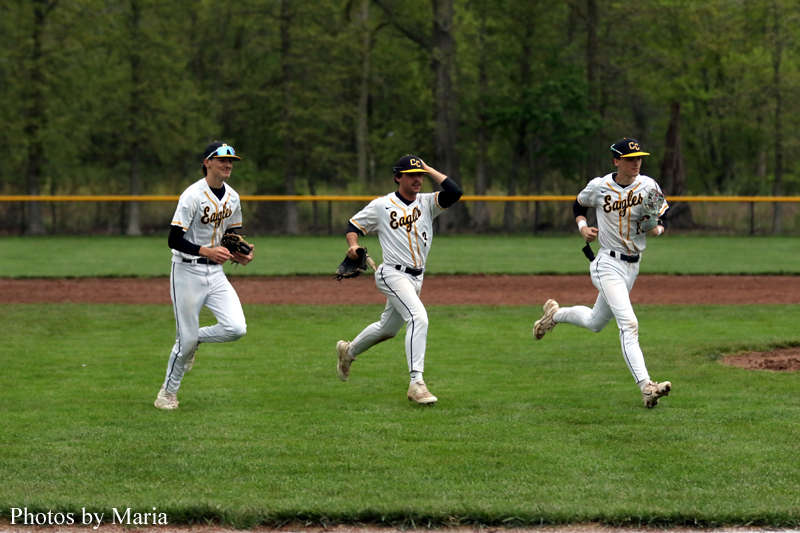 Three baseball players in white Eagles uniforms run across the outfield grass during a game.