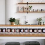 Row of small labeled jars on a wooden kitchen island in a bright, minimalist kitchen.
