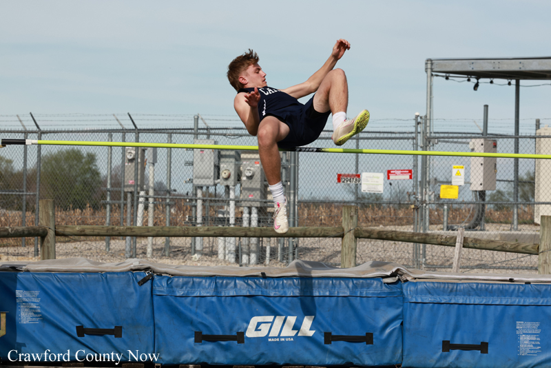 Male athlete mid-air clears a yellow high jump bar over a blue padded pit with 'GILL' branding in the foreground.