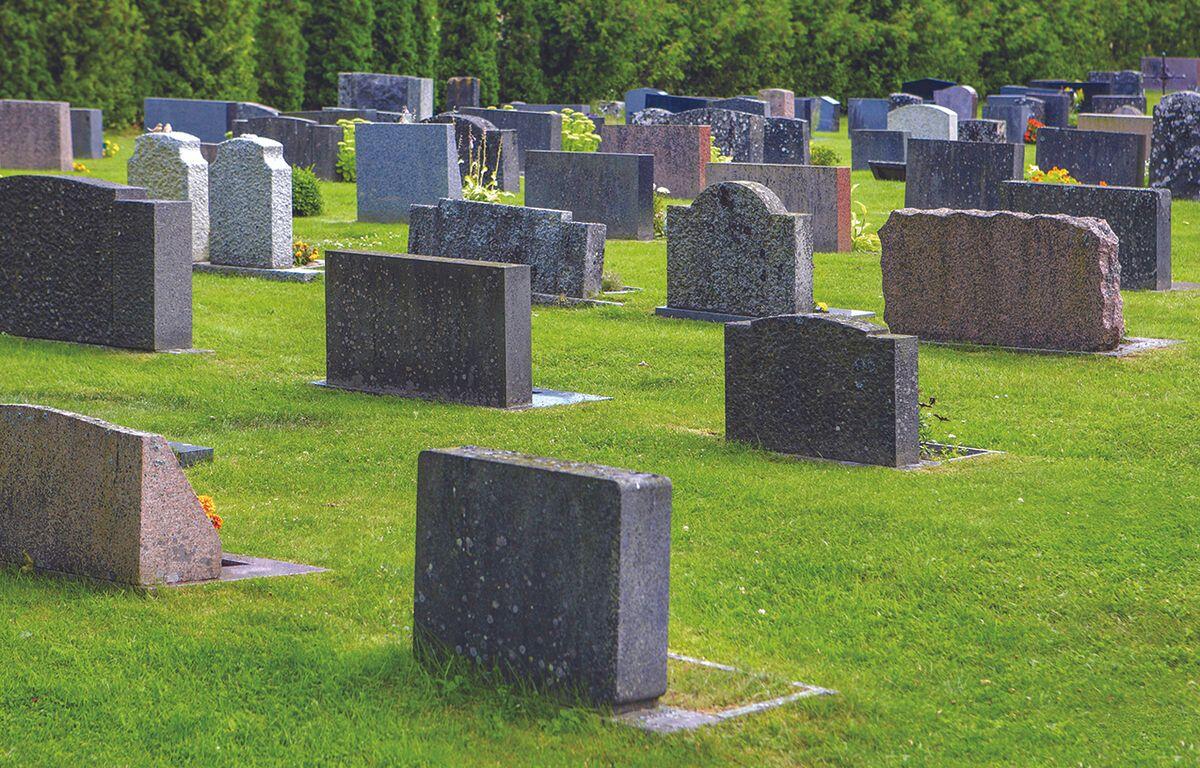 Grassy cemetery with numerous gray and brown tombstones arranged in rows beyond a green lawn.