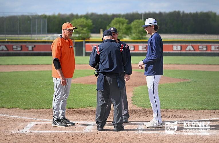 Three men stand at home plate on a baseball diamond, an umpire and two players in discussion during a game or practice.