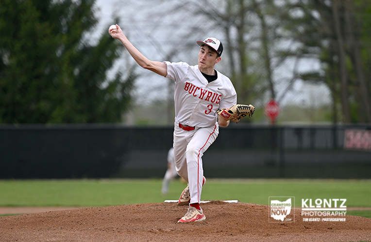 Baseball pitcher in a white uniform with red accents delivering a pitch from the mound on a grassy field.