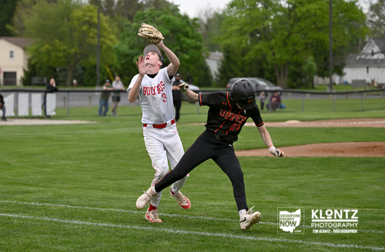 Baseball players battle near first base: white-jersey player reaches for the ball as black-jersey runner slides in.