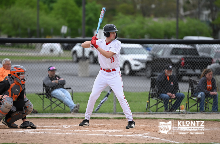 Baseball batter in a white uniform with red trim swings at a pitch, helmet on and bat raised.