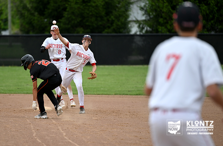 Baseball action scene: a white-uniform fielder throws while a black-uniform baserunner advances near third, with a blurred white‑uniform player in the foreground.