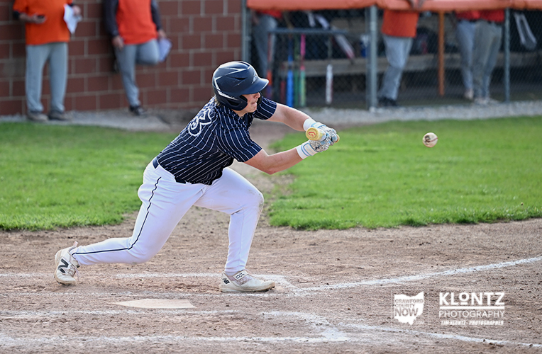 Baseball player in a navy pinstripe jersey bunting at home plate, helmet on, ball in midair