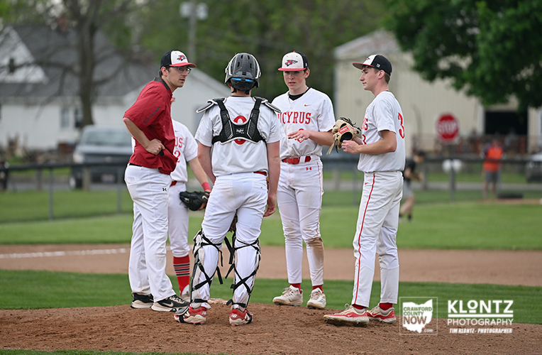 A group of baseball players in white uniforms circle around the catcher on the infield during a game.
