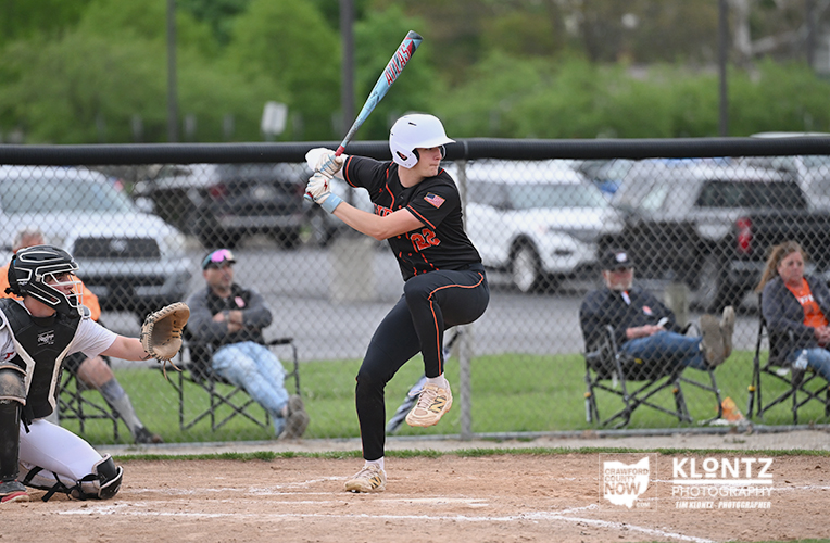 Female softball player in a white helmet swings at a pitch during a game, with catcher ready behind.