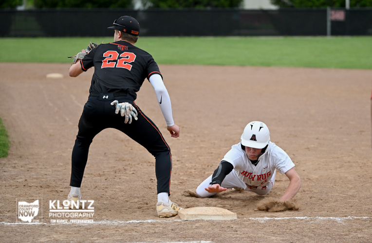 Baseball play at a base: fielder in black jersey number 22 stands over the base while a runner in white slides in, kicking up dirt.