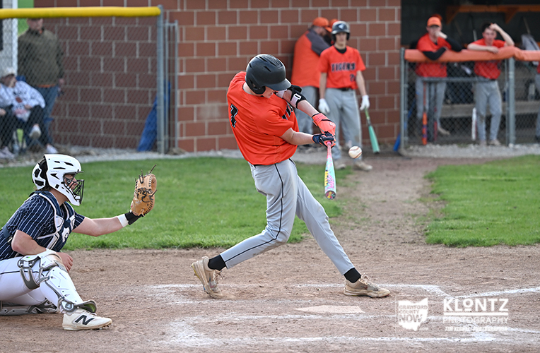 Youth baseball: batter in red swings and makes contact as catcher crouches behind home plate in a blue uniform.”)