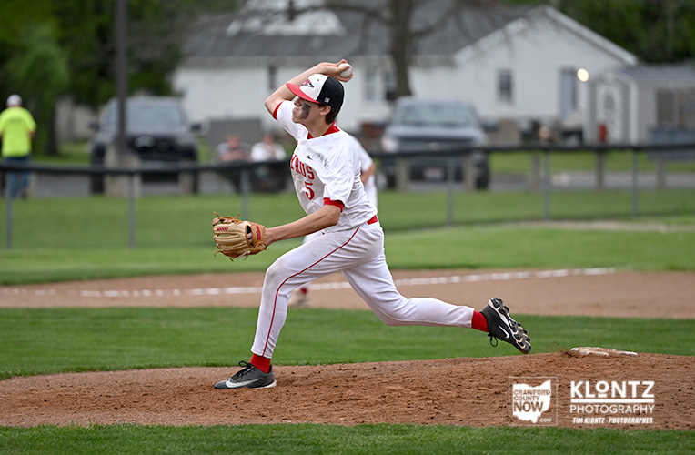 Right-handed baseball pitcher in white and red uniform throwing a pitch from the mound on a grass field.