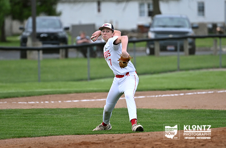 Baseball pitcher in white uniform throwing from the mound on a grassy field, red accents and glove up ready to throw.