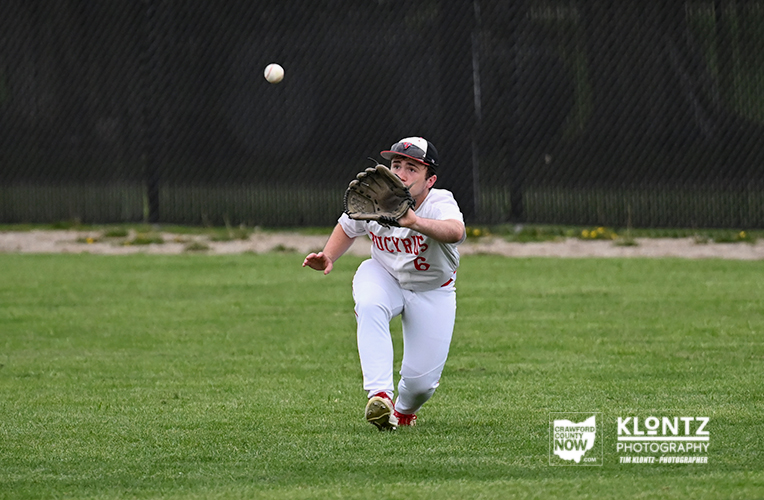 Baseball player in white uniform lunges to catch a high ball with a glove on a grassy field.
