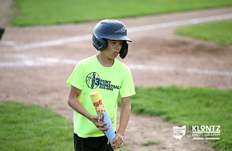 Young baseball player in a bright neon shirt and helmet holding a bat on a field with grass and dirt in the background.