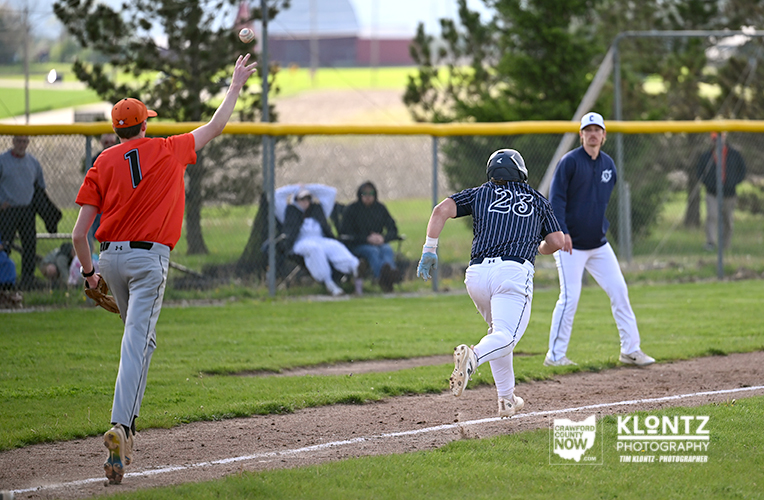 Baseball scene: a fielder in orange reaches for a high throw as a runner in a striped uniform (#23) sprints toward first base with spectators behind the fence.