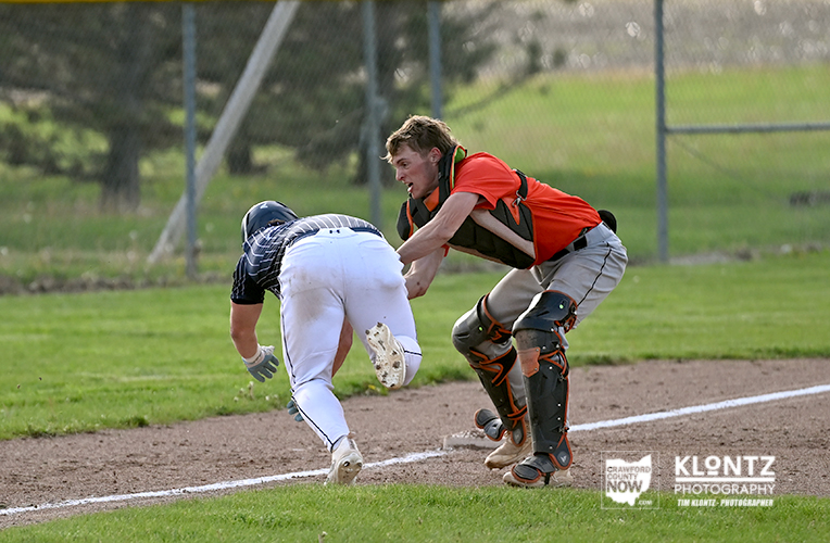 Baseball catcher in orange protective gear tags a sliding baserunner near the baseline on the infield dirt.
