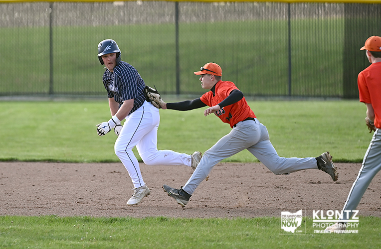 Baseball action: a baserunner in a blue-striped uniform advances on the dirt as an orange-uniform fielder reaches with his glove.