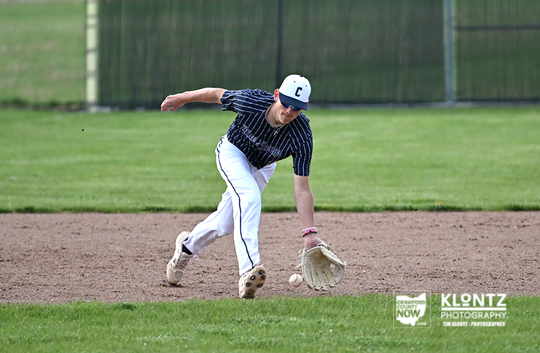 Baseball infielder in navy pinstripe uniform scoops a ground ball on a dirt infield.