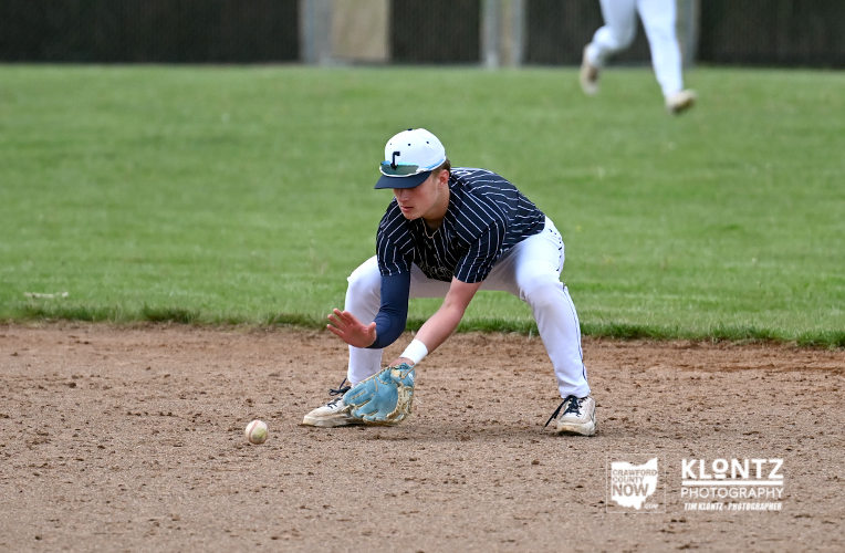 Baseball fielder in a navy pinstripe jersey crouches to field a ground ball on the infield dirt.