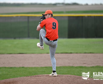 Right-handed baseball pitcher in an orange uniform (number 9) delivering a pitch from the mound on a grassy field.