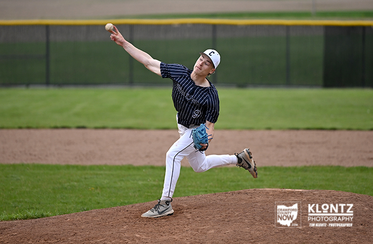 Baseball pitcher mid-throw from the mound, wearing a navy pinstripe uniform and white cap with a C logo, on a green field.