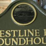 Green signboard with gold embossed lettering that reads 'CRESTLINE PRR ROUNDHOUSE' and a circular window at the top center, likely a railroad facility marker.