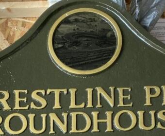 Green signboard with gold embossed lettering that reads 'CRESTLINE PRR ROUNDHOUSE' and a circular window at the top center, likely a railroad facility marker.