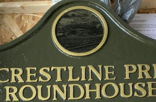 Green signboard with gold embossed lettering that reads 'CRESTLINE PRR ROUNDHOUSE' and a circular window at the top center, likely a railroad facility marker.