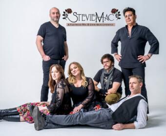 Group portrait of six people posing in a studio with a light backdrop; a StevieMac logo appears above them as a Fleetwood Mac & Stevie Nicks tribute act promo image.