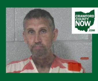 Mugshot of a man with short gray hair in an orange-striped jail uniform, posed against a gray cinder-block wall; Crawford County Now logo in the corner.