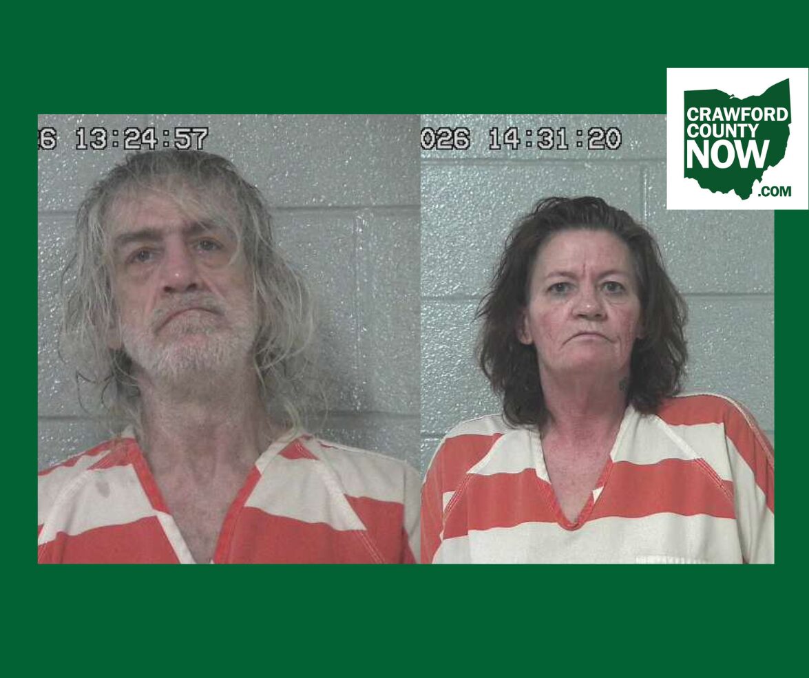 Two side-by-side mugshots: man with long gray hair and beard on the left, woman with dark hair on the right, both in orange-and-white striped jail uniforms against a gray cinder-block wall; timestamp overlays and Crawford County Now logo in corner.