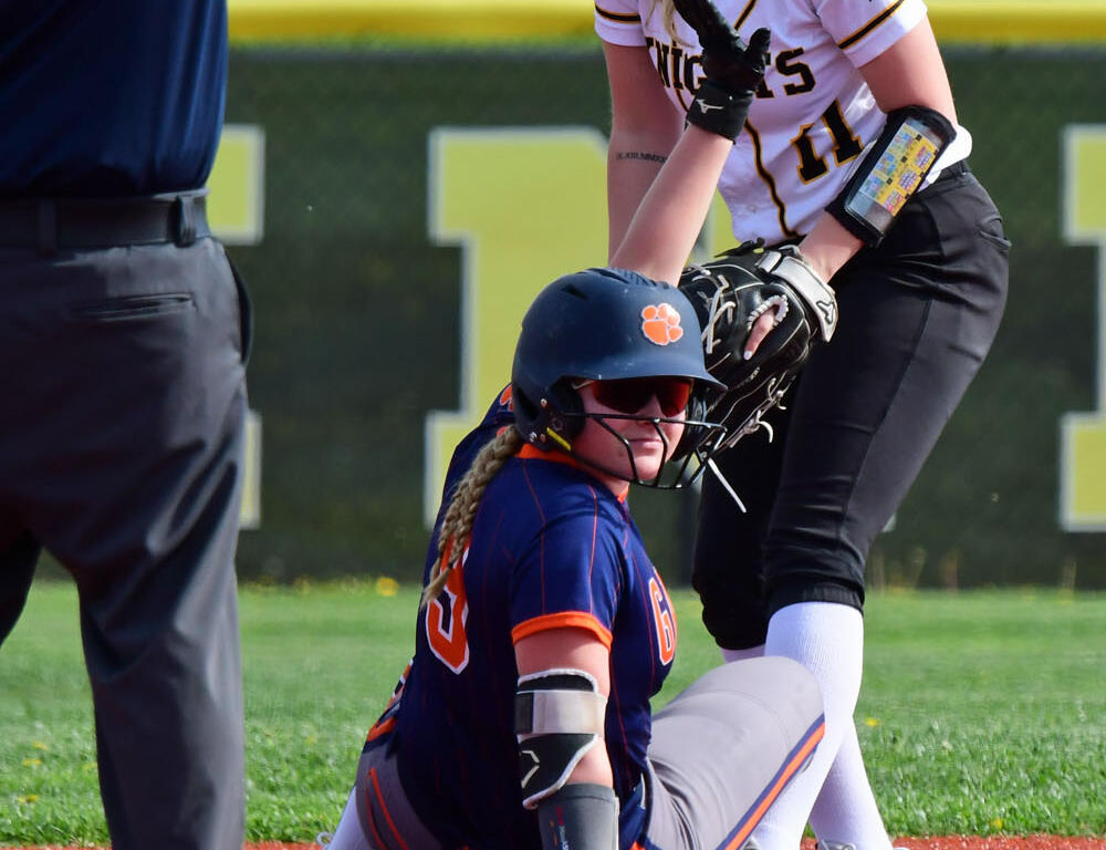 Female softball fielder in white uniform tags a sliding baserunner in blue and orange at the base.