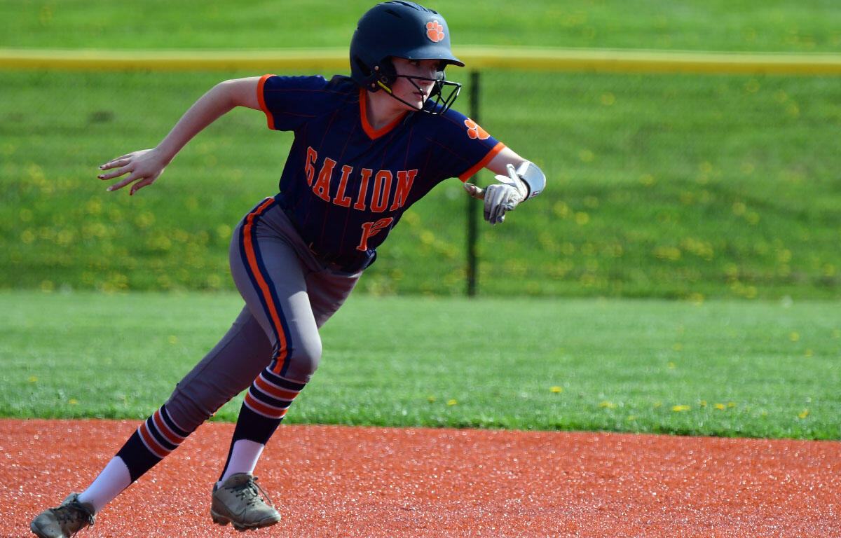Youth baseball player in navy and orange uniform sprinting on the infield dirt, helmet on, glove ready for a play on a sunny field.