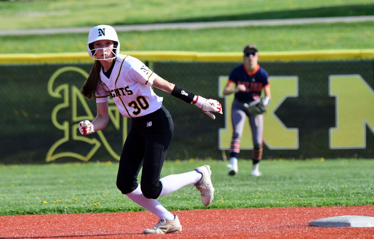 Softball player in white jersey number 30 runs on the infield, helmet on, glove ready, with a teammate in the background near the field fence.