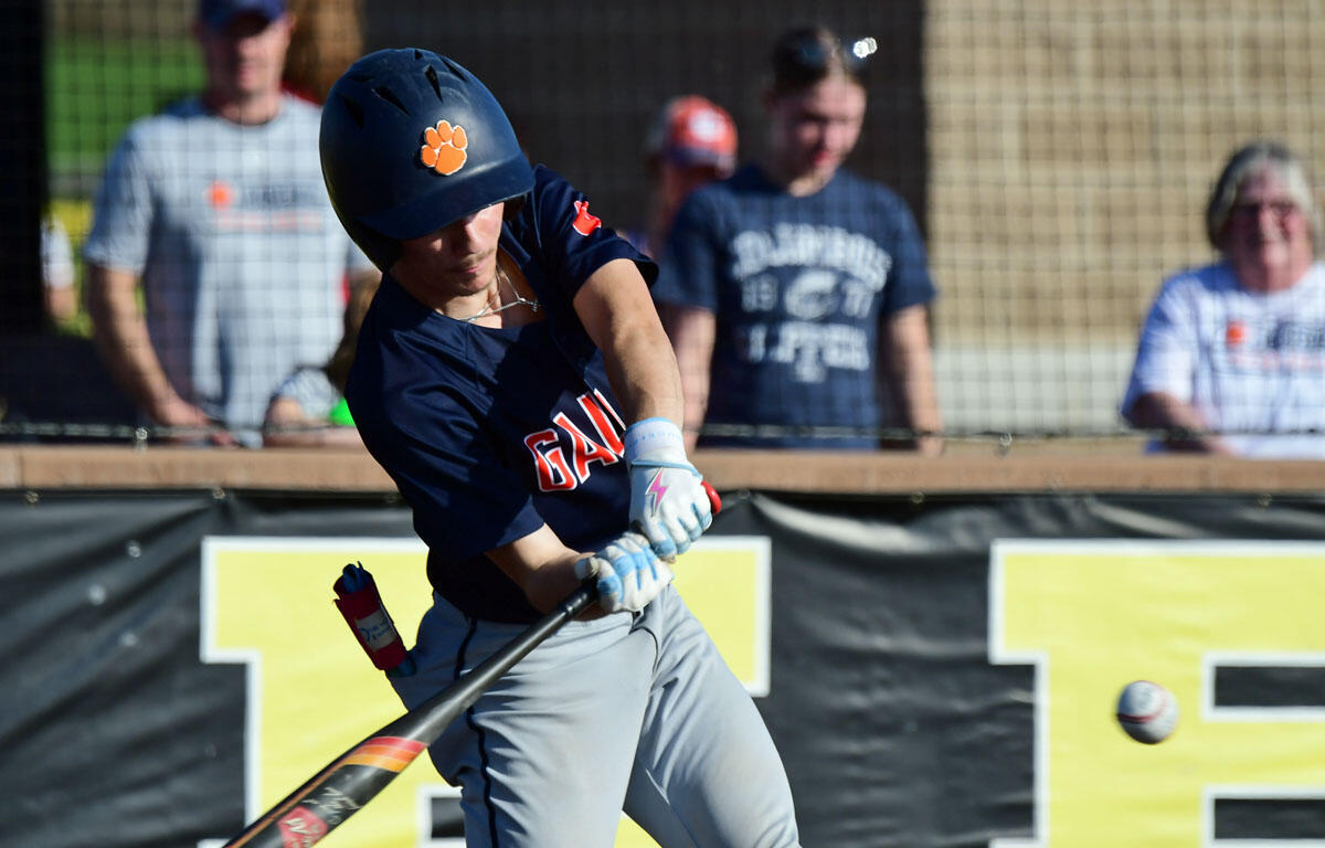Baseball batter in a navy uniform swings a bat, helmet with an orange paw print visible.