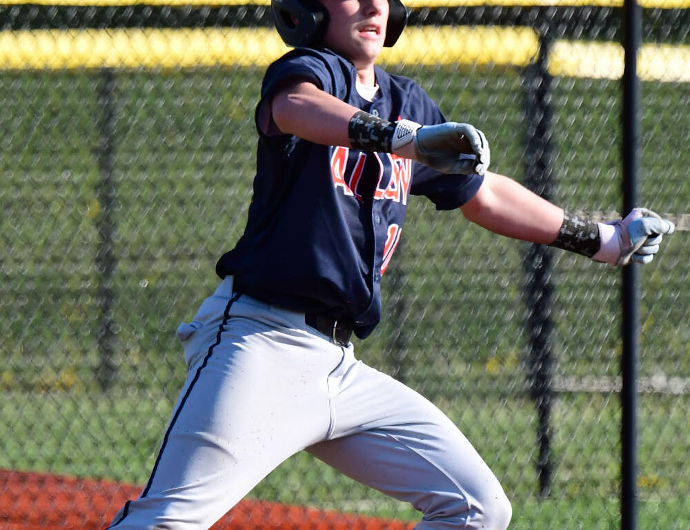 Young baseball player in a navy jersey and gray pants runs on a baseball field, wearing a helmet and batting gloves.