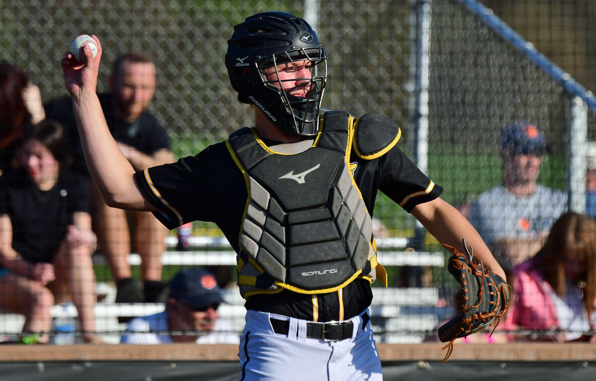 Baseball catcher in black and yellow gear throws a ball during a game.