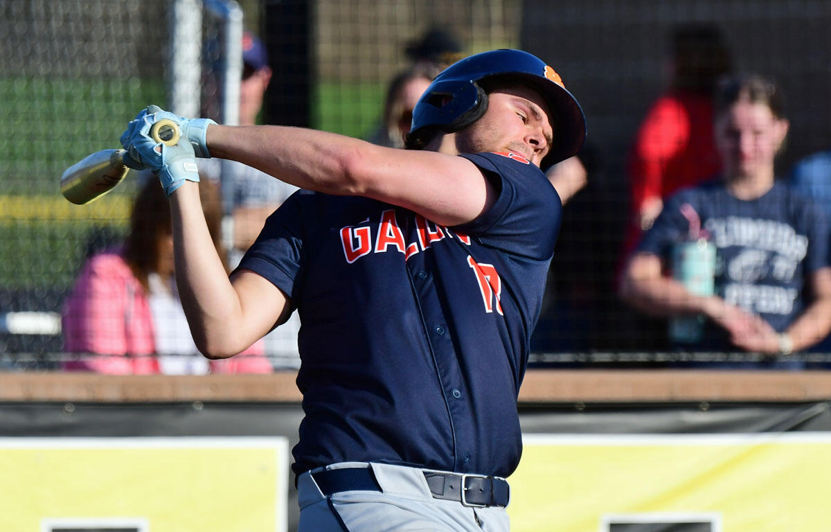 Baseball player in navy uniform swinging a bat during a game, helmet on, crowd behind him on a fence-lined field