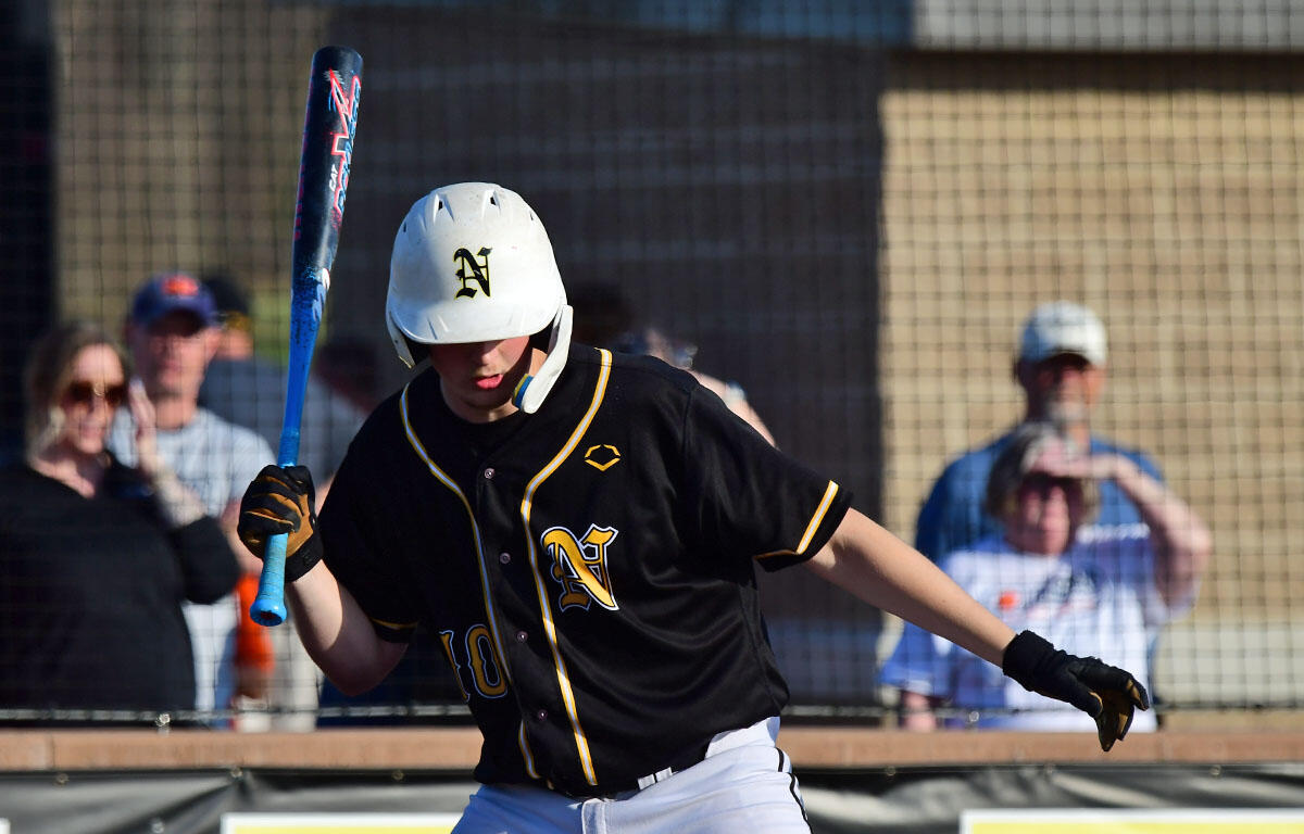 Baseball player in a black and gold jersey swings a blue bat during a game, wearing a white helmet with an N logo.