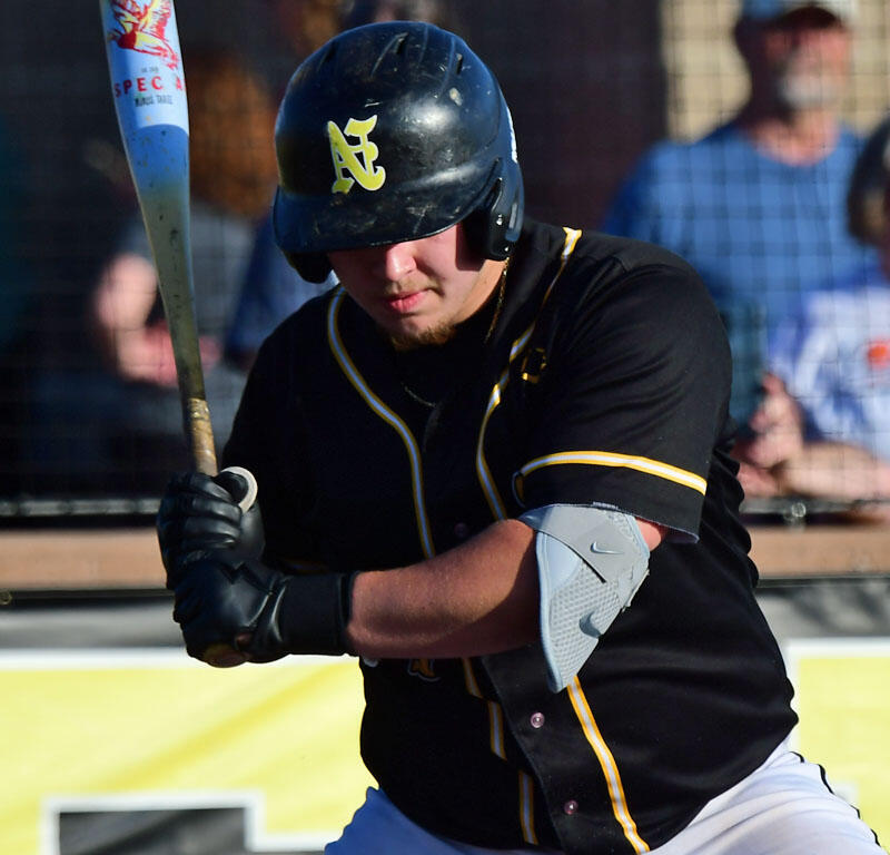 Baseball batter in black uniform with yellow piping swings at a pitch, helmeted and focused.