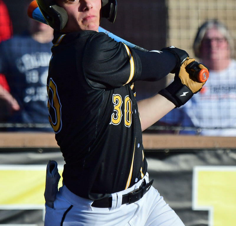 Baseball player in black and yellow uniform stops mid-swing, wearing helmet and batting gloves, number 30 visible, hitting during game outdoors.