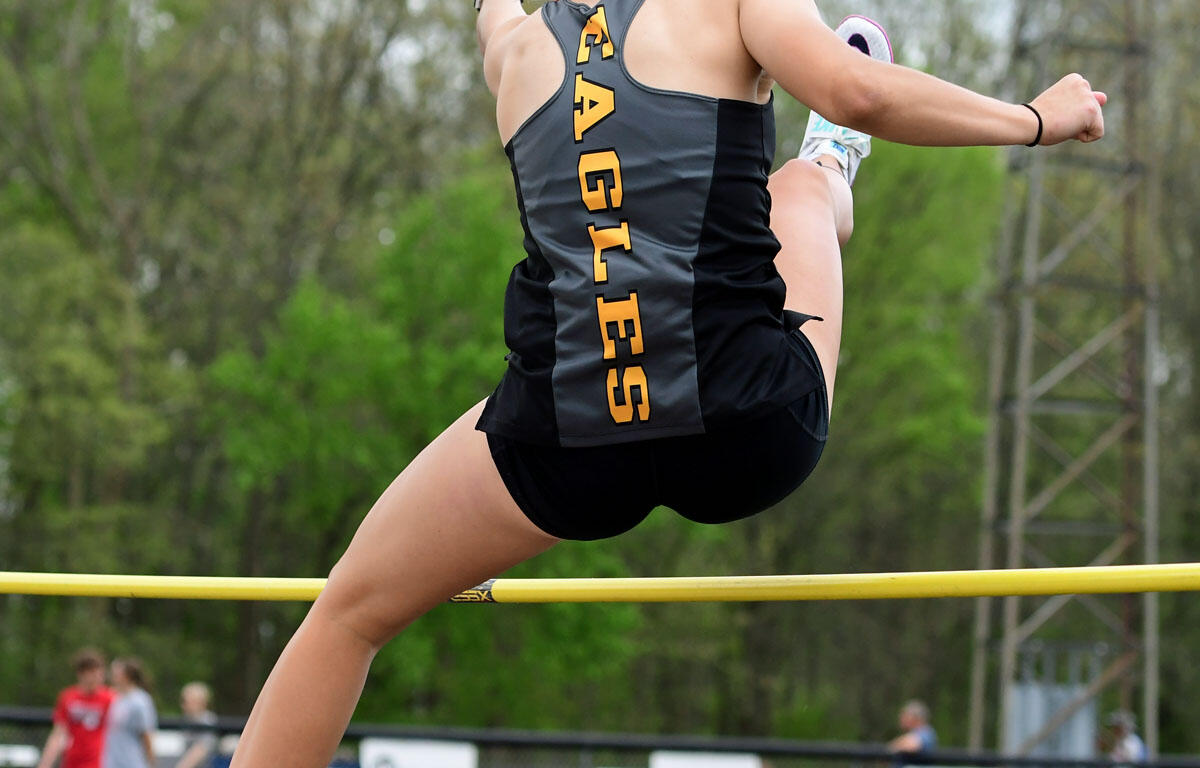 Female high jumper in gray and black uniform with 'EAGLES' on the back, mid-air clearing a yellow bar outdoors