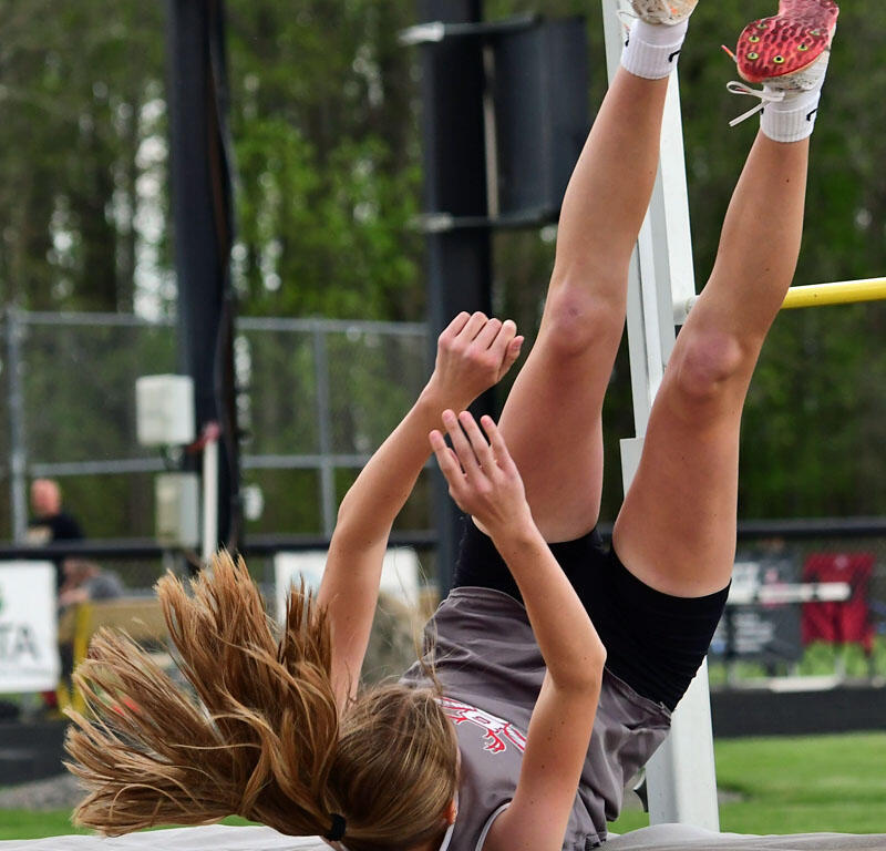 Athlete performs a high jump, feet up near the bar, landing on a padded mat during a track and field event.