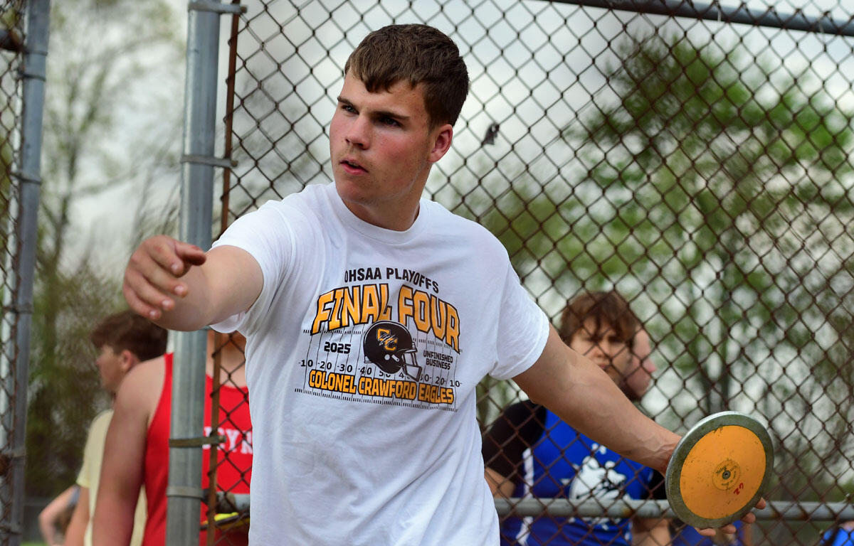 Young man in a white t-shirt throws a yellow frisbee during an outdoor game in front of a chain-link fence.