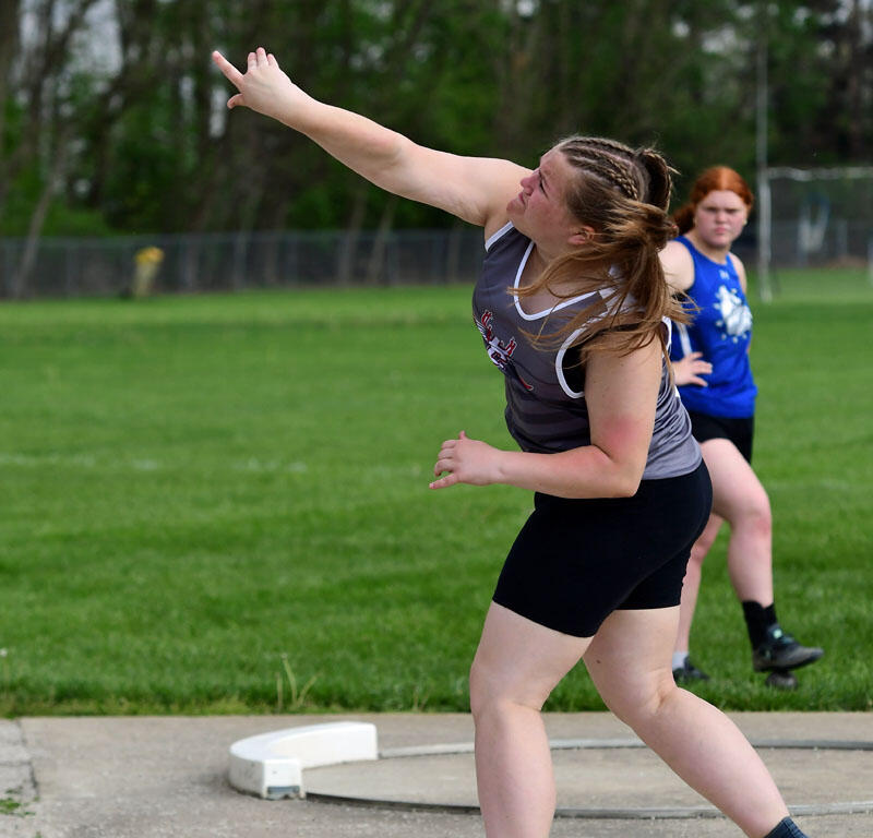 Woman in athletic gear throwing a hammer in a field event, mid-swing with a metal ball in the air on a throwing circle