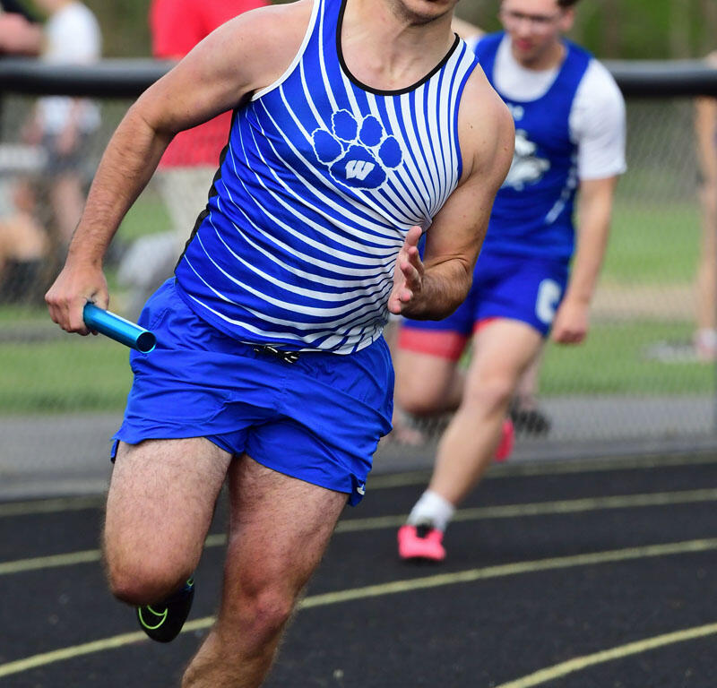 Male sprinter wearing blue and white striped jersey, holding a blue baton while running on a track on a relay race.