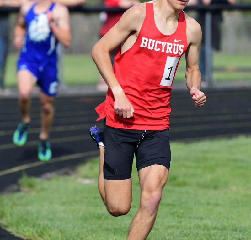 Male sprinter in a red Bucyrus jersey (no. 1) running on a track during a race, wearing white sunglasses and black shorts.