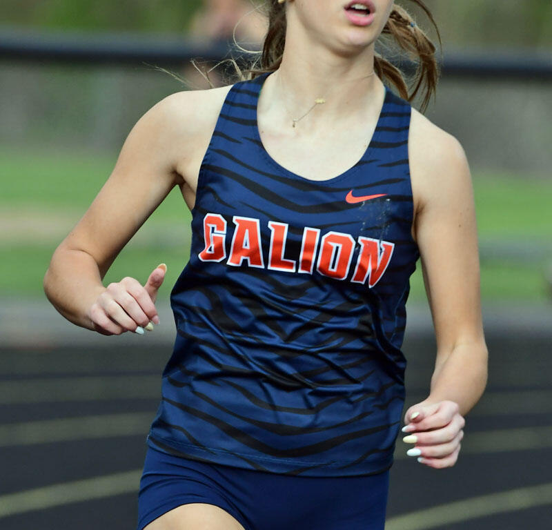 Female sprinter on a track, wearing a navy blue Galion uniform with orange lettering, mid-race and focused.
