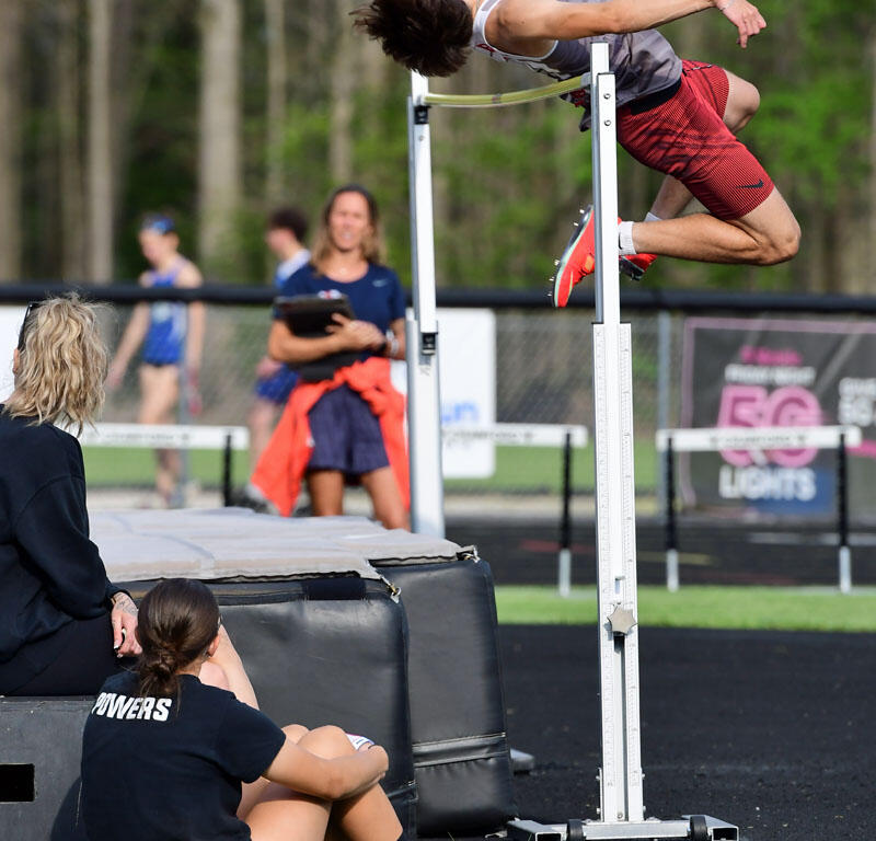 Male high jumper clears the bar during a track and field event, landing mat and bystanders in the background.