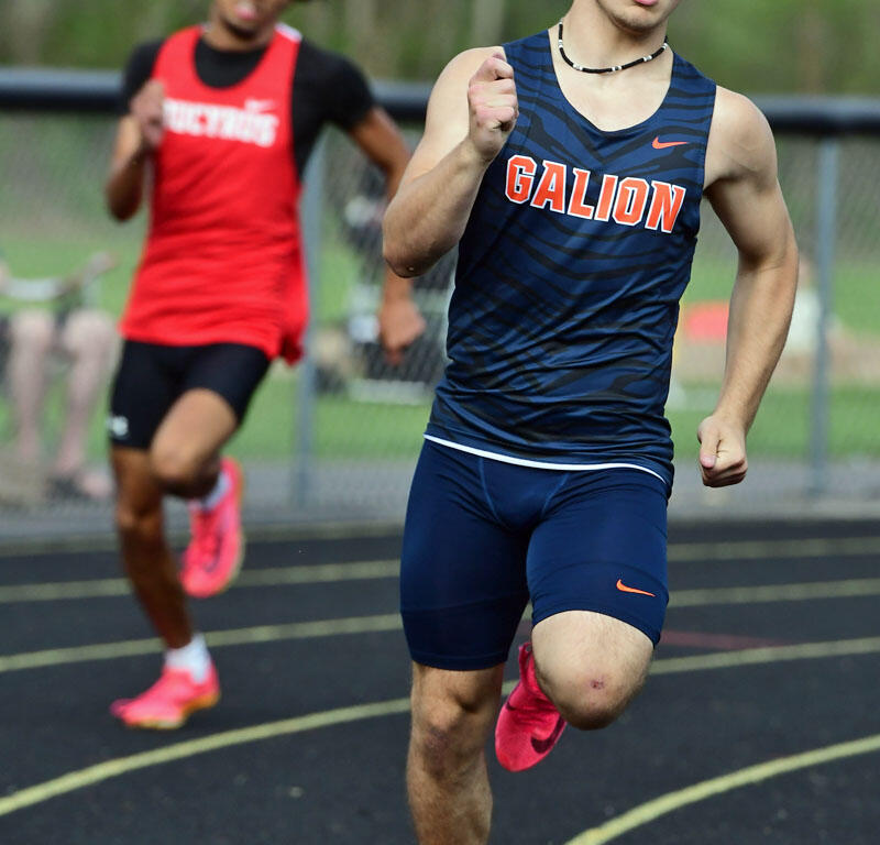 Front-running sprinter in a navy Galion uniform with pink shoes powers down the track as a blurred competitor in red follows behind on an outdoor track.